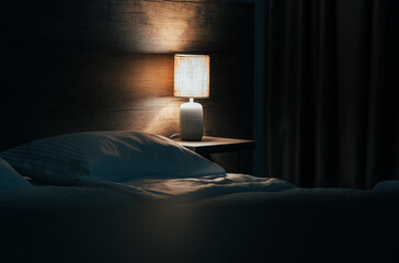 The cozy bed in the hotel at night with yellow night lamp. The light from the lamp reflects on the wooden wall. Toned image with copy space for you text.