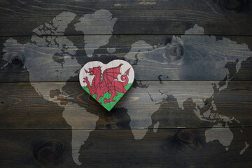 wooden heart with national flag of wales near world map on the wooden background.