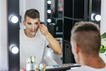 Man looking in the mirror while doing his makeup with a sponge in the dressing room.