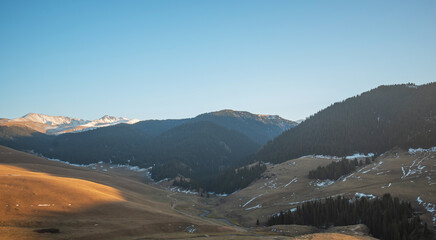 Dusk light illuminates a mountainous landscape, highlighting a winding valley with sparse snow and...