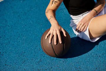 A young woman with tattoos sits on the ground holding a basketball, exuding an aura of...