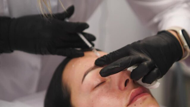 Beauty clinic. Beautician hands in gloves making face aging injection in a female skin. A woman gets beauty facial cosmetology procedure. Botox. collagen injections. Shot in 4k