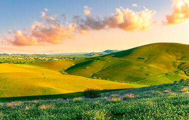 spring or summer beautiful landscape of green hills and flowering meadow with fields and mountains and amazing cloudy sunset sky on backgeound