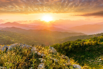 highland mountain landscape of beautiful sunset or sunrise with nice mountain peaks and slopes, green and golden hills and majestic cloudy sky on background