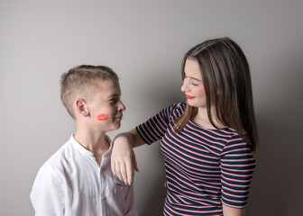 Girl and boy with lipstick kiss on his face on bright background.