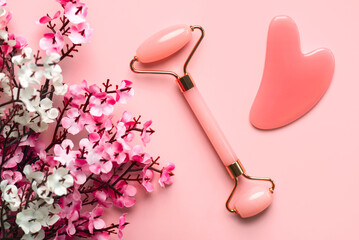 Closeup of pink jade roller, jade gua sha massager stone and almond blossoms. Skin care products concept