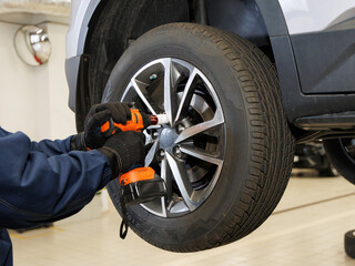 Car mechanic worker doing tire or wheel replacement with pneumatic wrench in garage of repair service station