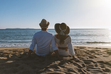 Happy couple in love, is seating on the beach during sunset or sunrise. Summer vacations.