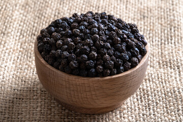 Black peppercorns in wooden bowl on burlap sack