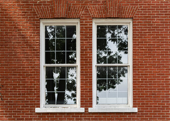 Reflection of light on vertically oriented white-framed rectangular windows on a red brick wall,...