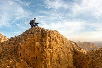 Man hiker sitting on top of a rocky mountain looking at the view