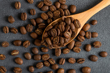A spoon full of roasted coffee beans on black background,top view