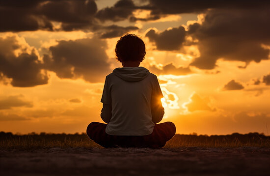 Prayer concept. Silhouette of a black boy child in a praying pose. Set against a vibrant sunset sunrise sky. Clasped hands. Also related to reverent, inner, uplifting, radiance, sacred