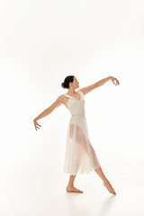 Fototapeta na wymiar A young woman exudes grace as she moves in a white dress in a studio setting against a white backdrop.