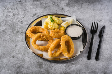 Fried calamari with potato salad next to it on stone table