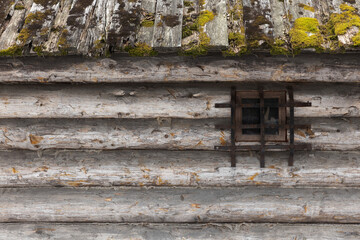 Old wooden house roof with green moss and wall made of rough gray logs
