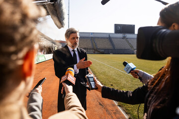 Interview of private investor at press conference for TV news in soccer stadium. Director of football team answering press questions and giving interview. Inspirational speech during press campaign. - obrazy, fototapety, plakaty