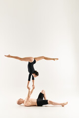 Fototapeta na wymiar Shirtless young man and dancing woman defy gravity in a synchronized handstand pose against a white studio backdrop.