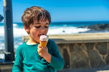 A young boy is eating an ice cream cone on a beach