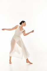 A young woman exudes elegance and grace as she dances in a flowing white dress in a studio setting against a white background.
