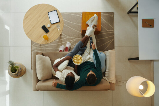 Young couple eating popcorn and watching tv at home, view from the top