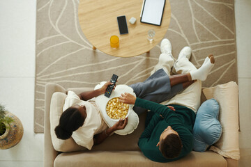 Couple sitting on comfy sofa, eating popcorn and watching new tv show