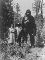 Old vintage aged mystery photograph of a man and woman standing with a giant bigfoot cryptid sasquatch creature in the forest