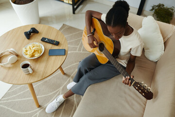 Black young woman learning playing guitar at home - 782091227