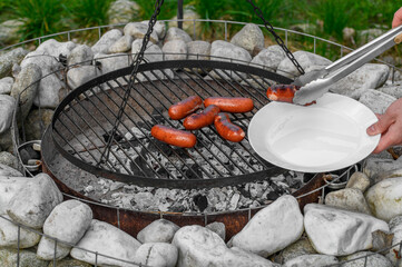 Grill w ogrodzie, nakładać gorące mięso - wypieczone kiełbaski na talerz