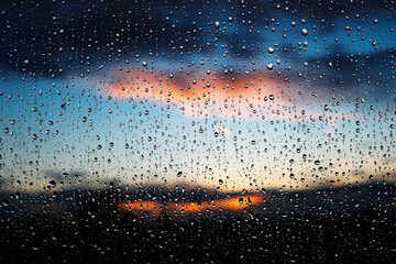 Stunning photoshoot of raindrops on a window with background of sunset in the sky. Wallpaper image with water drops and blurred sky and clouds on the background - obrazy, fototapety, plakaty