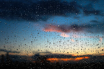 Stunning photoshoot of raindrops on a window with background of sunset in the sky. Wallpaper image with water drops and blurred sky and clouds on the background