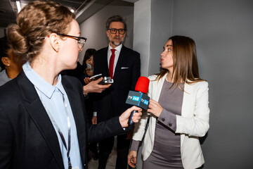 Confident female politician answers press questions and gives interview to the media walking in hallway of government building. Busy diplomat surrounded by crowd of news journalists. Press conference.
