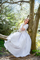 beautiful blonde smiling romantic bride in a white dress walking in blossoming magnolia garden on...