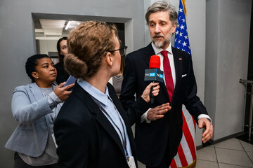 Confident American politician walks in corridor of government building, answers press questions and gives interview to the media. Busy diplomat surrounded by journalists. Press campaign. Slow motion. - obrazy, fototapety, plakaty