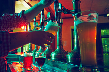 Male hand, bartender pouring foamy lager beer from tap into glass. Bar,, pub worker serving beer...