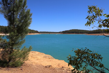 Logue Brook Dam (Lake Brockman) dam wall seen over turquoise colored water. Framed with trees.