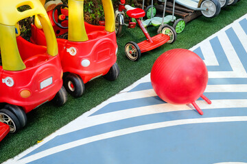 Colorful playground equipment with red toy cars and a ball on artificial turf 