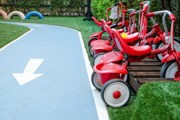 Red tricycles line up beside a track in a children's playground area