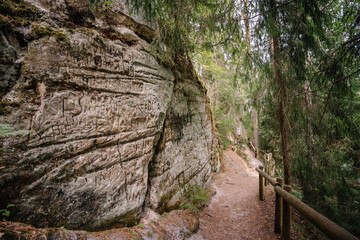 Valmiera, Latvia - July 14, 2023 - a forested pathway alongside a sandstone cliff with etched inscriptions and graffiti leads through Gauja National Park, Latvia, known as Sietiniezis.
