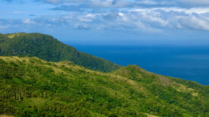 Aerial view of the mountain range of a tropical island. Mountains and hills of a tropical island covered with jungle against the backdrop of the blue sea.