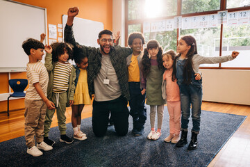 Primary school teacher celebrating with his students in a classroom - 782112869