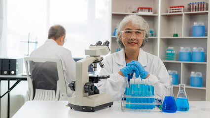 Asian senior male and female chemists examine test samples under a microscope. and his assistant...