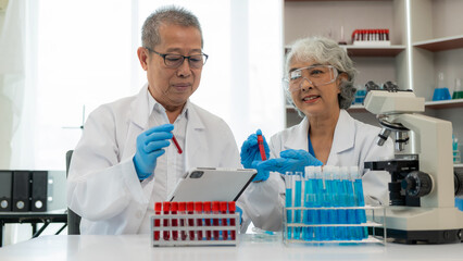 Asian senior male and female chemists examine test samples under a microscope. and his assistant...
