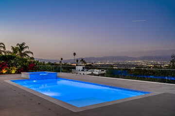 Empty swimming pool with city lights in the distance under a clear blue sky