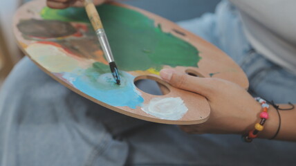 Cropped image of female artist standing in front of an easel and dipping brush into color palette