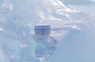 Jar of natural anti-aging cream for facial skin care during cold season. Advertising for nourishing restorative organic cosmetic on podium made of blue ice floes against backdrop of pile of ice floes