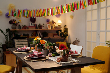 Table served with fresh exotic fruits, kitchenware and domestic flowers in flowerpots standing in the center of spacious living room
