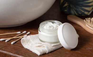 Opened cosmetic cream jar on folded towel near basin on wooden counterto in bath, lid mockup