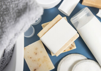 Soap bar with blank label near hygiene products on blue in bathroom top view, mockup
