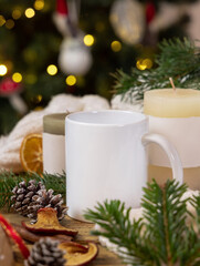 White coffee mug near Christmas decor, candles and fir twigs, cozy winter mockup